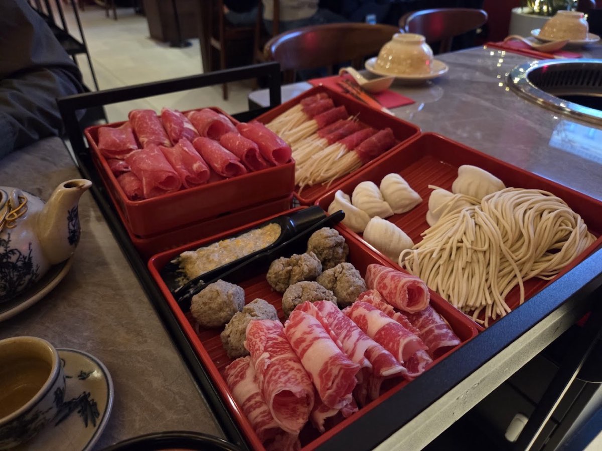 Czerwone lakierowane tace z rolkami mięsa, klopsikami i ręcznie robionym makaronem przy stole grillowym